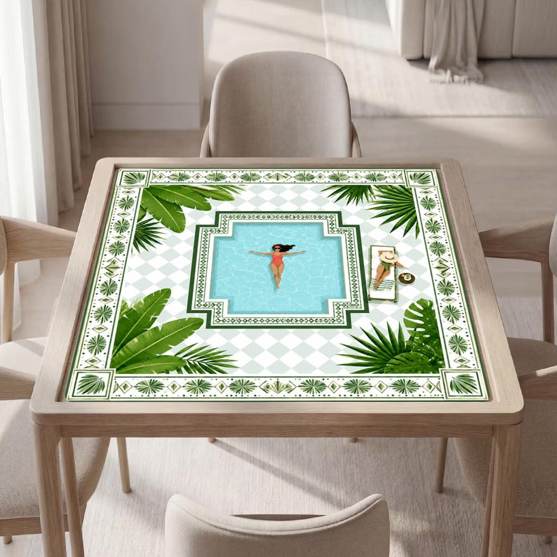 May include: A square table featuring a printed surface with a light blue swimming pool graphic, a person floating in the water, and another person on a lounge chair. The design includes green palm leaves and a white and light gray checkered pattern.