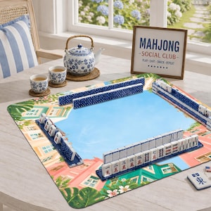 Puede incluir: Un juego de Mahjong con fichas blancas con caracteres rojos y negros sobre una alfombrilla de juego colorida con estampado de edificios tropicales. Una tetera de cer&aacute;mica azul y blanca y dos tazas a juego, junto a un letrero enmarcado que dice MAHJONG SOCIAL CLUB PLAY-CHAT-SNACK-REPEAT.