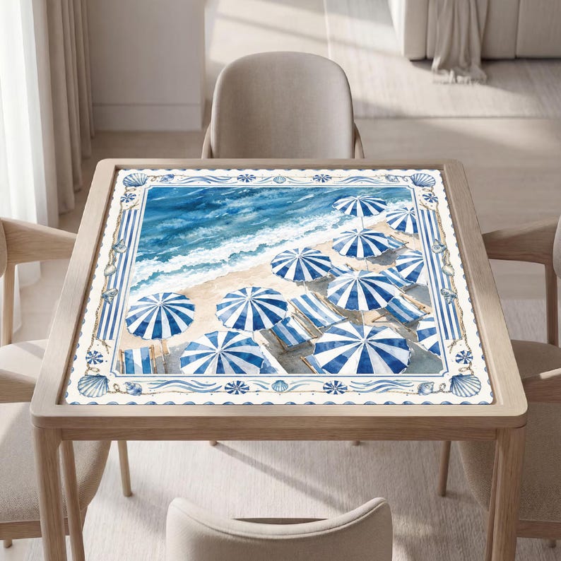 May include: A square table cover featuring a watercolor beach scene with blue and white striped umbrellas and lounge chairs on sand by the ocean. The border displays a repeating pattern of blue seashells and vertical stripes on a white background.