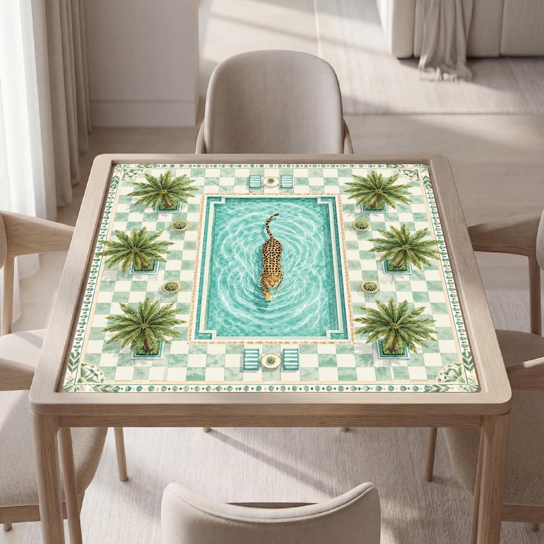 K&ouml;nnte beinhalten: Ein quadratischer Tisch mit einer Tischplatte, die eine gedruckte Illustration eines Swimmingpools zeigt. Das Design umfasst einen schwimmenden Leoparden in der Mitte, umgeben von Palmen und einem hellgr&uuml;n-wei&szlig;en Schachbrettmuster.