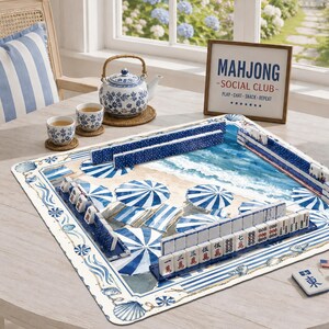 May include: A square mahjong mat featuring a beach scene with blue and white umbrellas, accompanied by a blue and white floral teapot, two matching teacups, and a framed sign that reads MAHJONG SOCIAL CLUB PLAY-CHAT-SNACK-REPEAT.