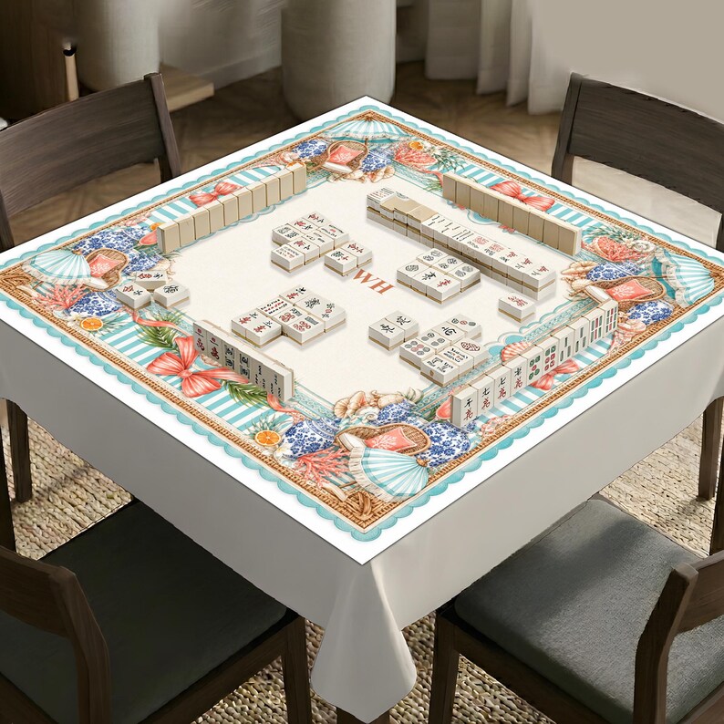 May include: A square mahjong table cover featuring a coastal-themed border with illustrations of beach umbrellas, coral, and red bows. The center is cream-colored with the letters WH and several sets of mahjong tiles arranged in rows and groups.