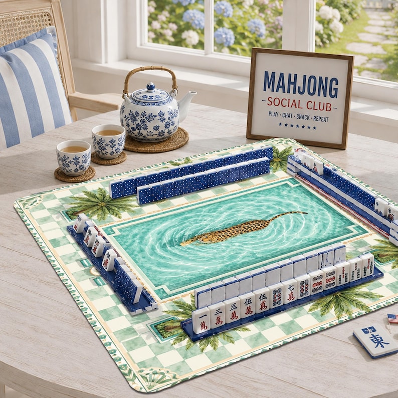 K&ouml;nnte beinhalten: Ein Mahjong-Set mit einer rechteckigen Spielmatte mit Schwimmbad- und Leopardenmotiv, blau-wei&szlig;en Spielsteinen, einer Keramik-Teekanne, zwei passenden Tassen und einem Schild mit der Aufschrift MAHJONG SOCIAL CLUB PLAY-CHAT-SNACK-REPEAT.