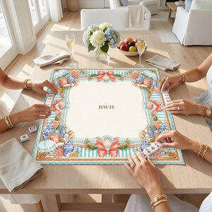 May include: A square mahjong mat featuring a cream-colored center with the letters RWH in the middle, surrounded by a decorative border of blue and white stripes, coral, seashells, wicker chairs, and red bows on a light blue and white background.