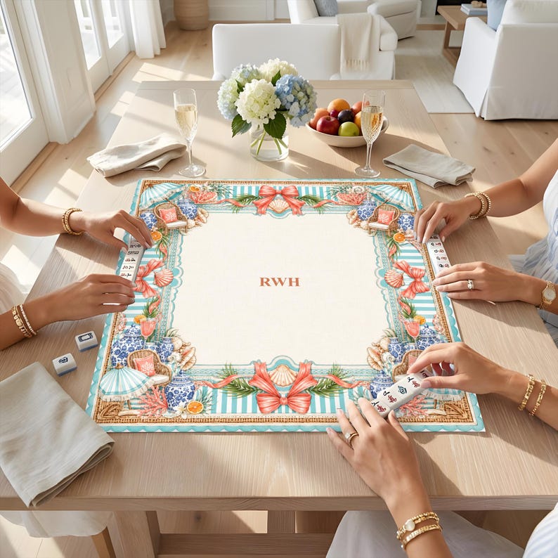 May include: A square mahjong mat featuring a cream-colored center with the letters RWH in the middle, surrounded by a decorative border of blue and white stripes, coral, seashells, wicker chairs, and red bows on a light blue and white background.