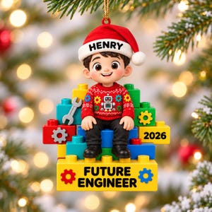 May include: A Christmas ornament featuring a cartoon boy wearing a red Santa hat with the name HENRY, a red jumper with a robot graphic, and black trousers. The boy sits on a stack of colourful building blocks with the text 2026 and FUTURE ENGINEER.