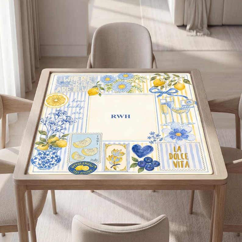May include: A square table mat featuring a cream-colored center with the monogram RWH in blue. The border displays blue and yellow stripes, lemons, blue flowers, a blue heart, wine glasses, and text including Where skies are blue, Italy, and La Dolce Vita.