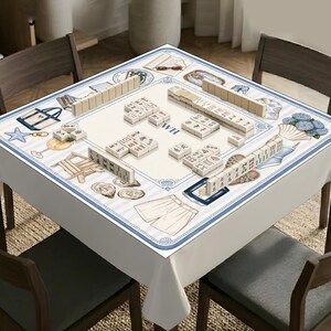 May include: A square mahjong table cover featuring a light blue and white striped border with illustrations of beach items like tote bags, starfish, seashells, and shorts. The center is cream-colored with the letters WH and scattered mahjong tiles.