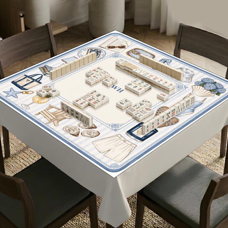 May include: A square mahjong table cover featuring a light blue and white striped border with illustrations of beach items like tote bags, starfish, seashells, and shorts. The center is cream-colored with the letters WH and scattered mahjong tiles.