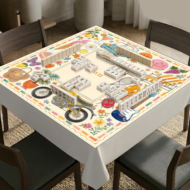 K&ouml;nnte beinhalten: Eine quadratische Mahjong-Tischdecke mit cremefarbenem Zentrum und einem Rand, der mit bunten Illustrationen von Motorrad, Gitarre, Marienk&auml;fer, Blumen, Fr&uuml;chten und Tennisschl&auml;ger verziert ist, mit Mahjong-Steinen auf der Oberfl&auml;che.