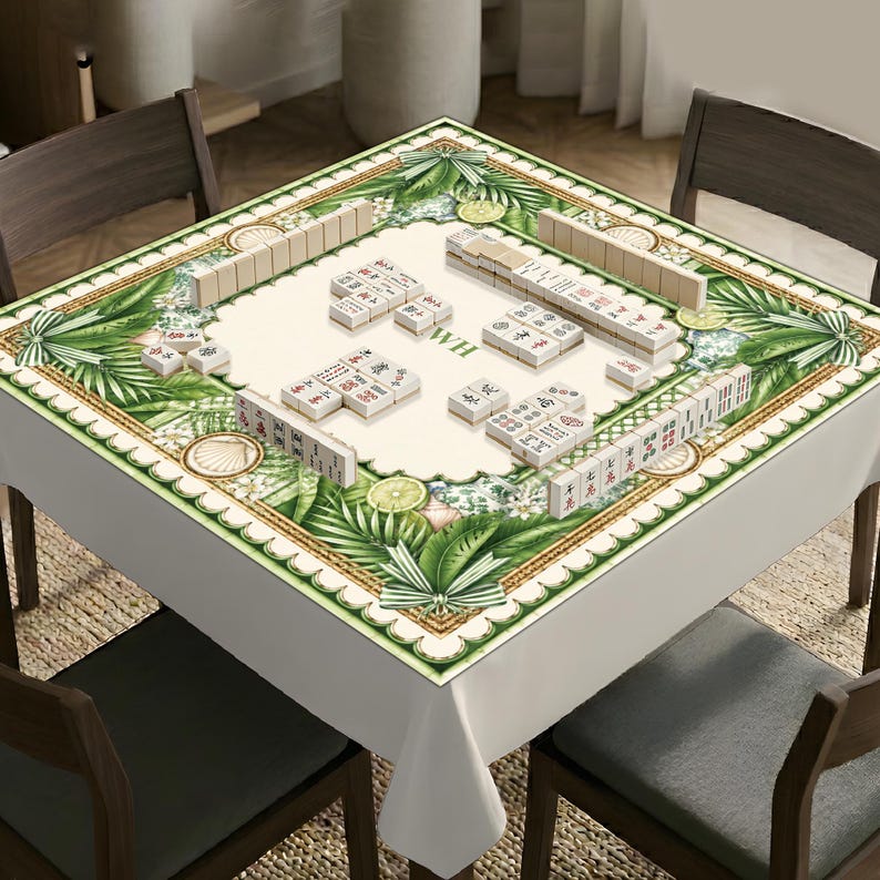 K&ouml;nnte beinhalten: Eine quadratische Mahjong-Tischdecke mit cremefarbener Mitte, auf der Mahjong-Steine und die Buchstaben WH liegen, umgeben von einem breiten Rand mit gr&uuml;nen Palmbl&auml;ttern, wei&szlig;en Bl&uuml;ten, Zitrusfr&uuml;chten und Muscheln auf wei&szlig;em Grund.