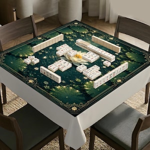May include: A square mahjong mat featuring a dark green background with a central white lotus flower and gold decorative borders. The mat is covered with white mahjong tiles arranged in various groupings, including long rows and small stacks.