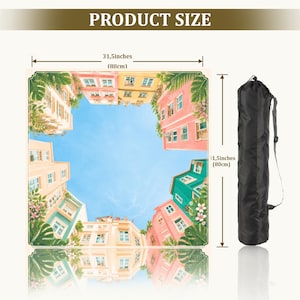 Puede incluir: Una alfombra cuadrada con una vista en contrapicado de edificios coloridos que rodean un cielo azul, con acentos de follaje verde. La alfombra mide 80 cm por 80 cm. Se muestra una bolsa de transporte cil&iacute;ndrica negra con correa al lado.