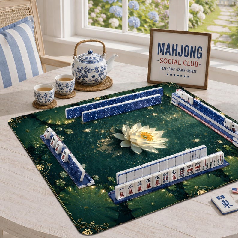 May include: A square mahjong mat with a dark green lotus pond print, featuring rows of white and blue mahjong tiles. A blue and white ceramic teapot and two matching teacups sit nearby, alongside a framed sign reading MAHJONG SOCIAL CLUB.