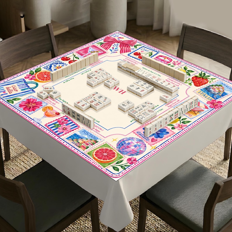 May include: A square mahjong table cover featuring a cream-colored center with game markings and the letters WH. The border displays a colorful collage of postage stamp-style illustrations including pink bows, cherries, strawberries, citrus, and disco balls.