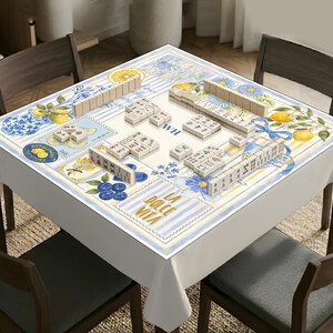 May include: A square mahjong table cover featuring a white background with blue and yellow stripes, floral patterns, lemons, and blueberries. The text reads "WHERE SKIES ARE BLUE", "WH", "OTTOLENGHI TEST KITCHEN", "Italy", and "LA DOLCE VITA".