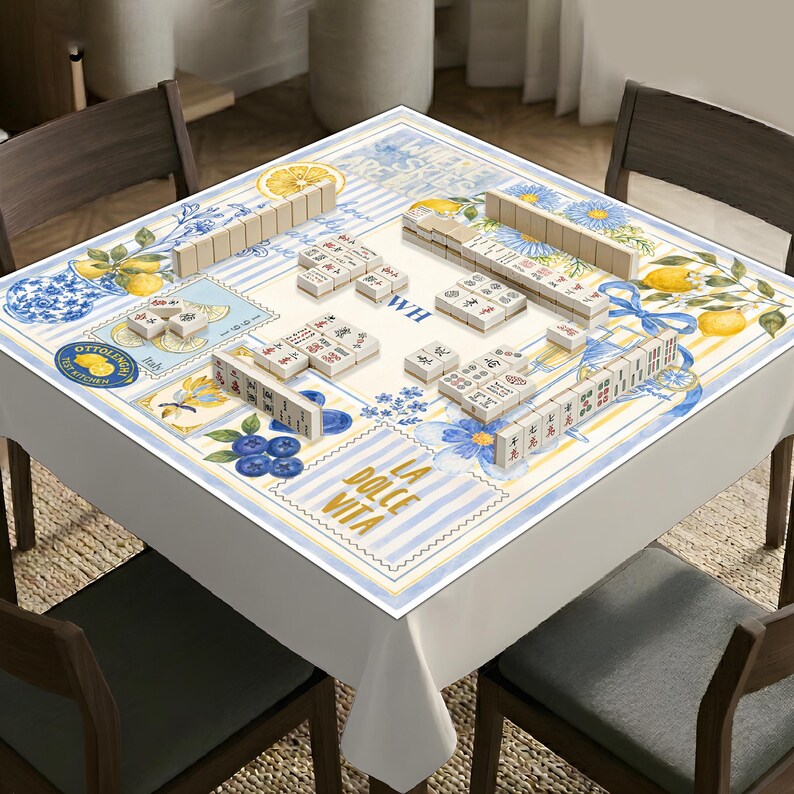 May include: A square mahjong table cover featuring a white background with blue and yellow stripes, floral patterns, lemons, and blueberries. The text reads "WHERE SKIES ARE BLUE", "WH", "OTTOLENGHI TEST KITCHEN", "Italy", and "LA DOLCE VITA".