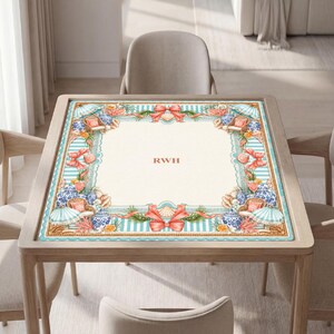 May include: A square table mat featuring a cream-colored center with the letters RWH in orange. The border displays a light blue and white striped pattern decorated with orange bows, seashells, blue and white vases, and beach umbrellas.