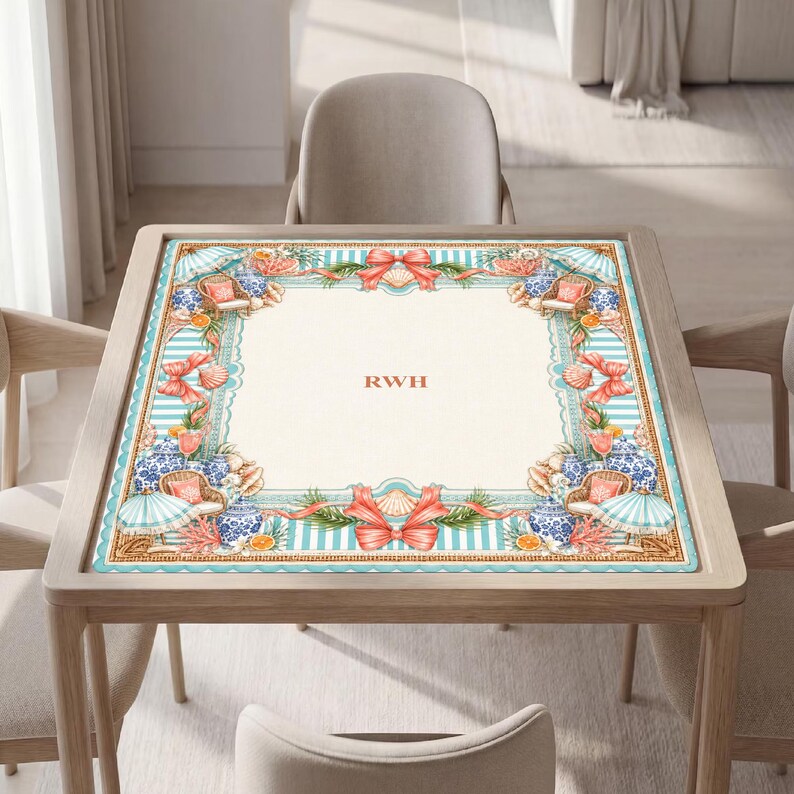 May include: A square table mat featuring a cream-colored center with the letters RWH in orange. The border displays a light blue and white striped pattern decorated with orange bows, seashells, blue and white vases, and beach umbrellas.
