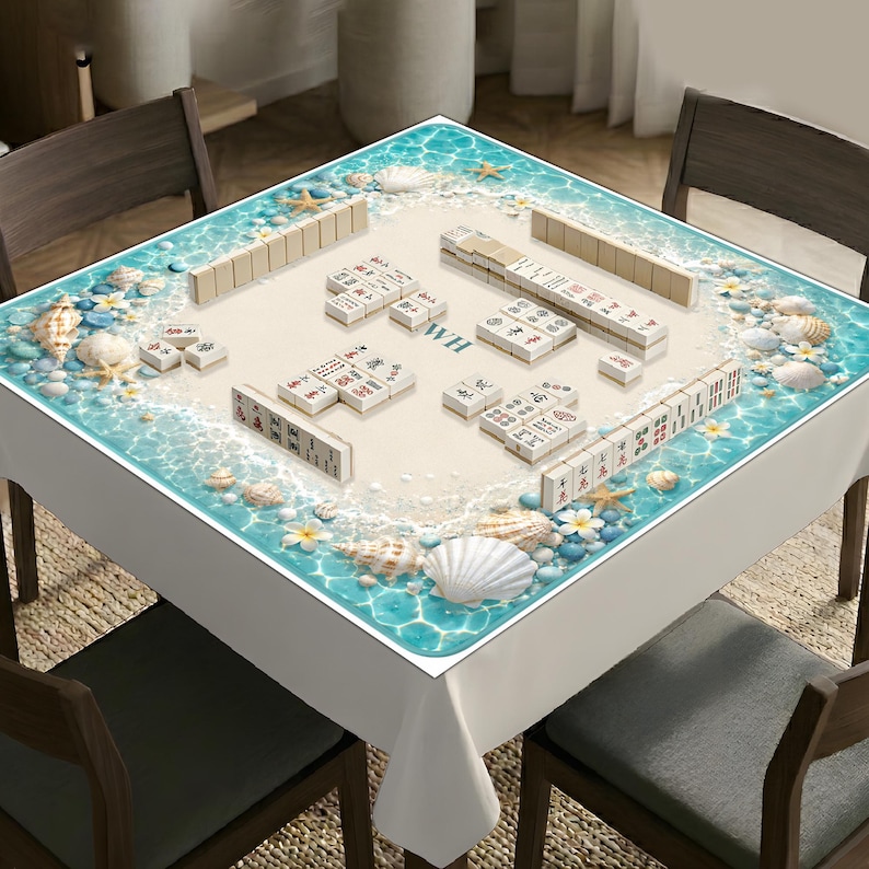 Puede incluir: Un mantel cuadrado con dise&ntilde;o de playa, agua turquesa, arena blanca, conchas y estrellas de mar. El centro muestra un juego de Mahjong con fichas dispuestas sobre la superficie, incluyendo las letras WH impresas en el medio.