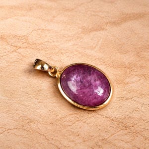 Peut inclure: Un pendentif doré avec une pierre précieuse ovale, violet foncé. La pierre est sertie dans un cadre doré et a une surface polie. Le pendentif a une petite boucle pour une chaîne.