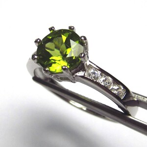 May include: A silver ring featuring a large green gemstone surrounded by smaller clear gemstones.