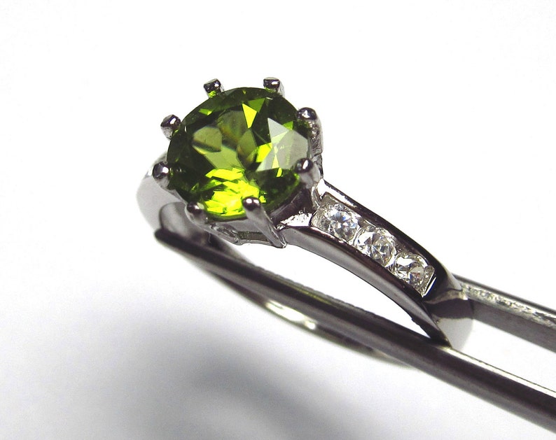 May include: A silver ring featuring a large green gemstone surrounded by smaller clear gemstones.