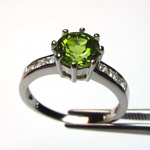 May include: A silver ring featuring a large green gemstone surrounded by smaller clear gemstones.