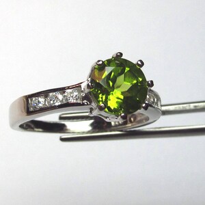 May include: A silver ring featuring a large green gemstone surrounded by smaller clear gemstones.