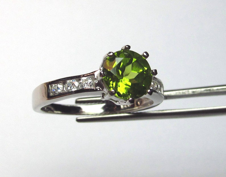 May include: A silver ring featuring a large green gemstone surrounded by smaller clear gemstones.