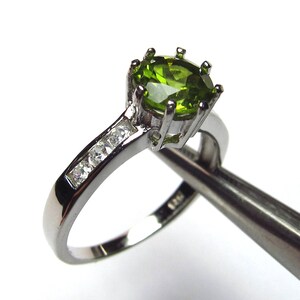 May include: A silver ring featuring a green oval gemstone and smaller clear gemstones on the band.