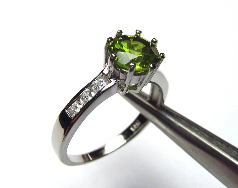 May include: A silver ring featuring a green oval gemstone and smaller clear gemstones on the band.