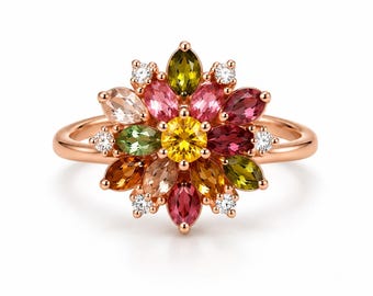 Puede incluir: Un anillo de oro rosa con una piedra preciosa central redonda de color amarillo rodeada por un grupo de piedras preciosas multicolores de talla marquesa, incluyendo tonos rosas, verdes, naranjas y marrones, con pequeñas piedras blancas claras.