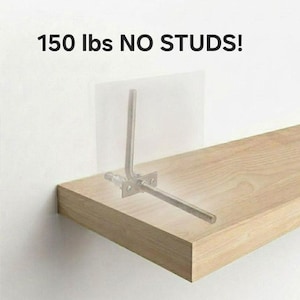 May include: A light-colored wooden shelf with a metal bracket and threaded rods is mounted on a white wall. The text "150 lbs NO STUDS!" is displayed above the shelf, indicating its weight capacity.