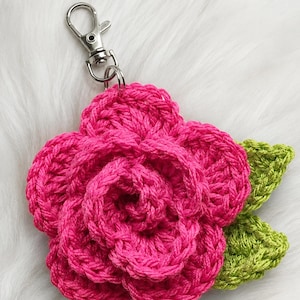 Peut inclure: Un porte-cl&eacute;s fleur au crochet compos&eacute; d'une rose rose vif aux p&eacute;tales superpos&eacute;s et de deux feuilles vert citron textur&eacute;es sur le c&ocirc;t&eacute;. Le motif floral est fix&eacute; &agrave; un mousqueton pivotant en m&eacute;tal de couleur argent&eacute;e.