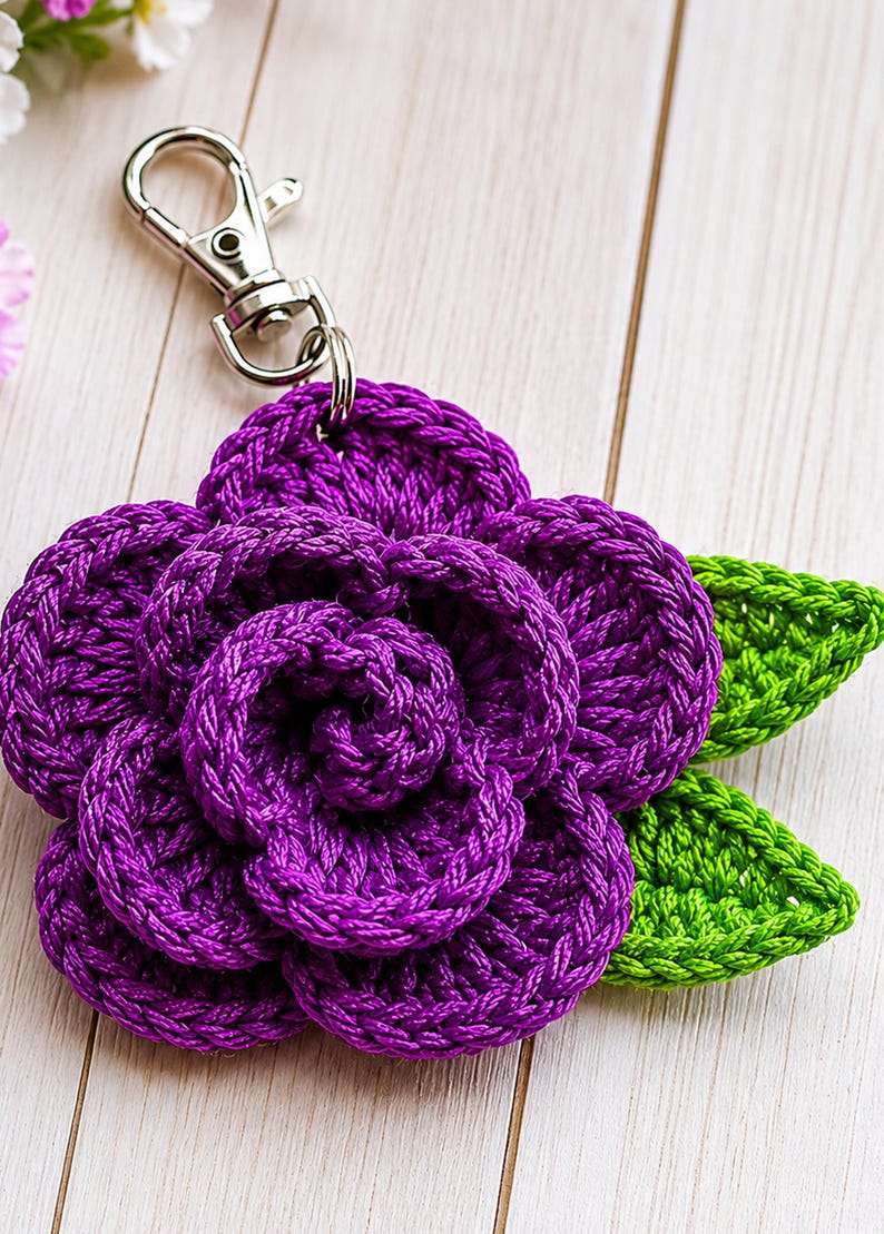 Peut inclure: Un porte-cl&eacute;s fleur crochet&eacute; violet pr&eacute;sentant un motif de rose &agrave; plusieurs couches avec deux feuilles crochet&eacute;es vert vif attach&eacute;es sur le c&ocirc;t&eacute;. La fleur est reli&eacute;e &agrave; un mousqueton en m&eacute;tal argent&eacute; par un petit anneau m&eacute;tallique.