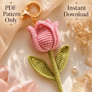 Può includere: Un portachiavi a forma di tulipano all'uncinetto con un fiore rosa e uno stelo verde con due foglie, fissato a un anello in metallo dorato. L'immagine include il testo PDF Pattern Only e Instant Download in un carattere decorativo.