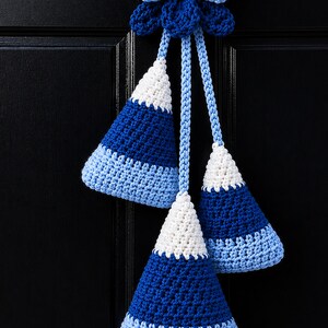 Pode incluir: Uma decora&ccedil;&atilde;o de croch&ecirc; suspensa com um la&ccedil;o azul-claro no topo, ligado a tr&ecirc;s ornamentos em forma de cone. Cada cone apresenta um padr&atilde;o de gradiente de cor que transita do branco no topo para o azul-escuro no meio e azul-claro na base.