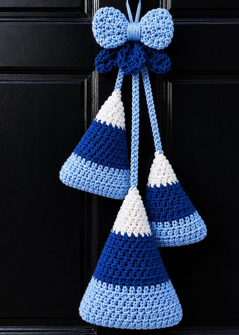 Pode incluir: Uma decora&ccedil;&atilde;o de croch&ecirc; suspensa com um la&ccedil;o azul-claro no topo, ligado a tr&ecirc;s ornamentos em forma de cone. Cada cone apresenta um padr&atilde;o de gradiente de cor que transita do branco no topo para o azul-escuro no meio e azul-claro na base.