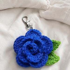 Peut inclure: Un porte-cl&eacute;s fleur en crochet compos&eacute; d'une fleur bleue aux p&eacute;tales superpos&eacute;s et de deux feuilles vert vif fix&eacute;es &agrave; la base. Le motif floral est reli&eacute; &agrave; un mousqueton en m&eacute;tal argent&eacute; pour une fixation facile sur des sacs ou des cl&eacute;s.
