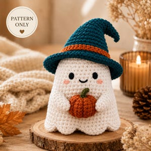 May include: A white crocheted ghost figure wearing a dark teal witch hat with an orange band. The ghost has black eyes, a small smile, pink cheeks, and holds a small orange crocheted pumpkin. A circular label reads PATTERN ONLY.