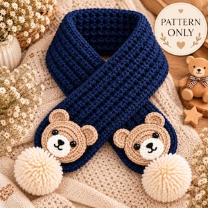 Può includere: Una sciarpa all'uncinetto blu scuro con due facce d'orso beige con occhi neri e musi bianchi, ciascuna rifinita con un pompon di filato color crema alle estremità. Un'etichetta circolare nell'angolo in alto a destra riporta il testo PATTERN ONLY.
