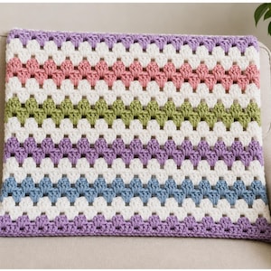 May include: A rectangular crochet blanket featuring a repeating granny stitch pattern. The design consists of horizontal stripes in alternating colors of light purple, white, dusty pink, white, sage green, white, light purple, white, and blue.