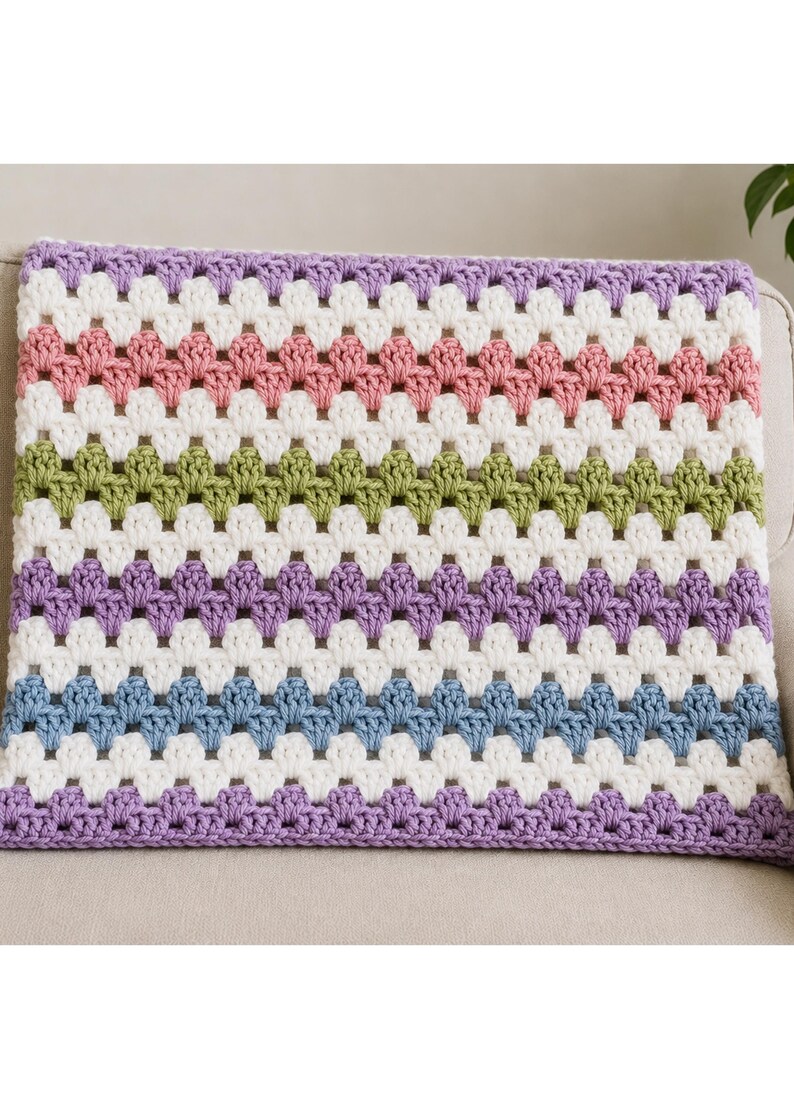 May include: A rectangular crochet blanket featuring a repeating granny stitch pattern. The design consists of horizontal stripes in alternating colors of light purple, white, dusty pink, white, sage green, white, light purple, white, and blue.