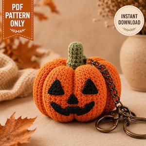 May include: A crocheted orange pumpkin keychain featuring a green stem and a black stitched jack-o'-lantern face with triangular eyes and a jagged mouth. The pumpkin is attached to a bronze-colored metal chain with a lobster clasp and ring.