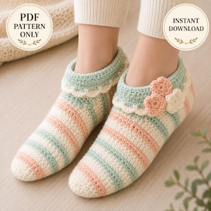 May include: A pair of crochet slippers featuring horizontal stripes in pastel peach, mint green, and cream. The slippers have a scalloped cuff edge and are decorated with three small, layered crochet flowers in peach and cream on the side.