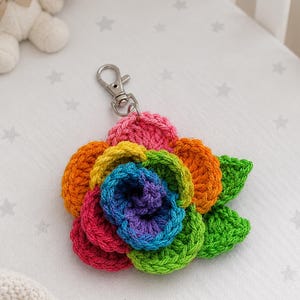 Peut inclure: Un porte-cl&eacute;s fleur en crochet multicolore avec des p&eacute;tales superpos&eacute;s dans des tons de rose, orange, jaune, vert, bleu et violet. La fleur est fix&eacute;e &agrave; un mousqueton en m&eacute;tal argent&eacute;, offrant un point d'attache fonctionnel pour les cl&eacute;s ou sacs.