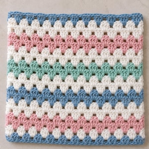 May include: A square crochet piece featuring a repeating granny stitch pattern. The design consists of horizontal stripes in alternating colors of light blue, cream, dusty pink, and mint green, creating a soft, multi-colored textile square.