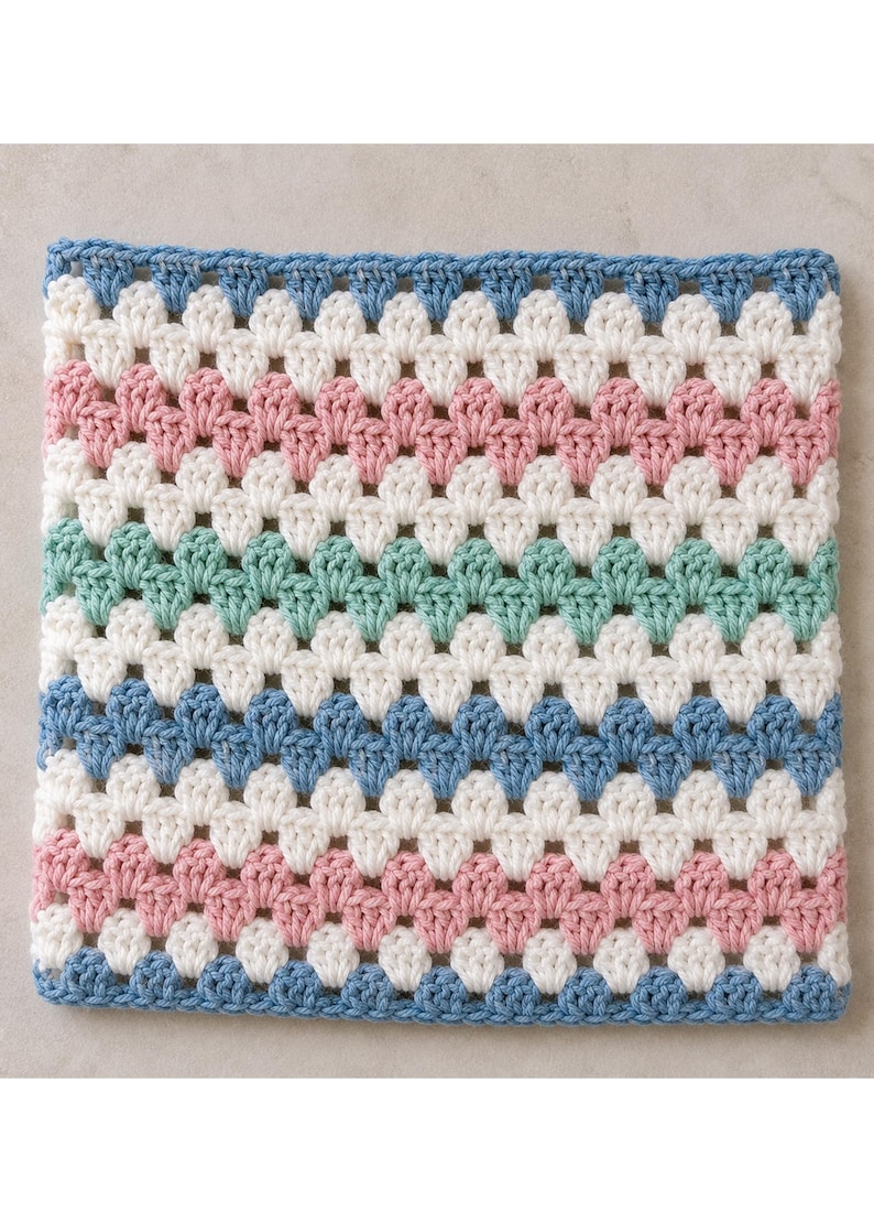 May include: A square crochet piece featuring a repeating granny stitch pattern. The design consists of horizontal stripes in alternating colors of light blue, cream, dusty pink, and mint green, creating a soft, multi-colored textile square.