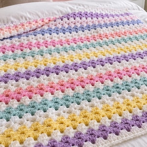 May include: A rectangular crochet blanket featuring a repeating granny square stitch pattern. The design consists of horizontal stripes in pastel shades of lavender, yellow, mint green, and soft pink, each separated by rows of white yarn throughout.